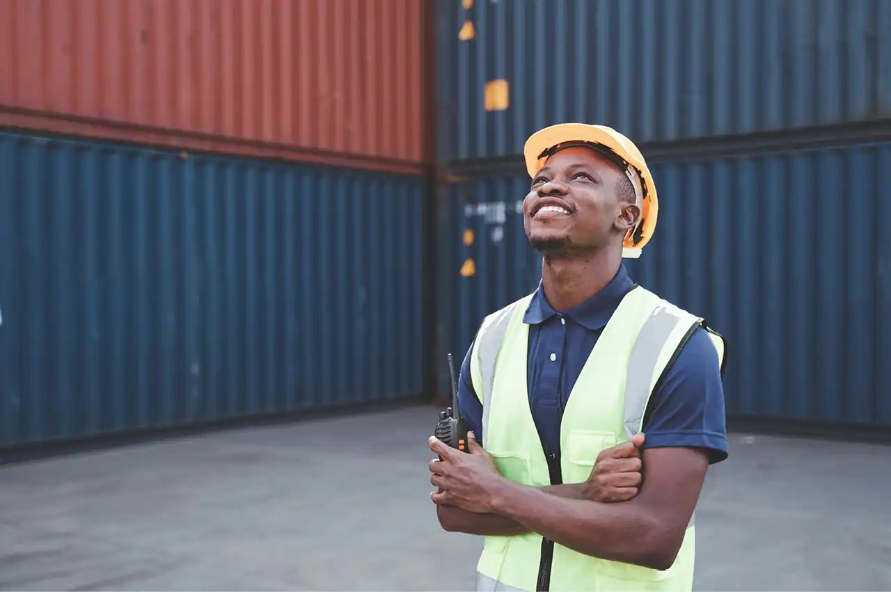 A container yard worker looking up at a stack of containers and smiling
